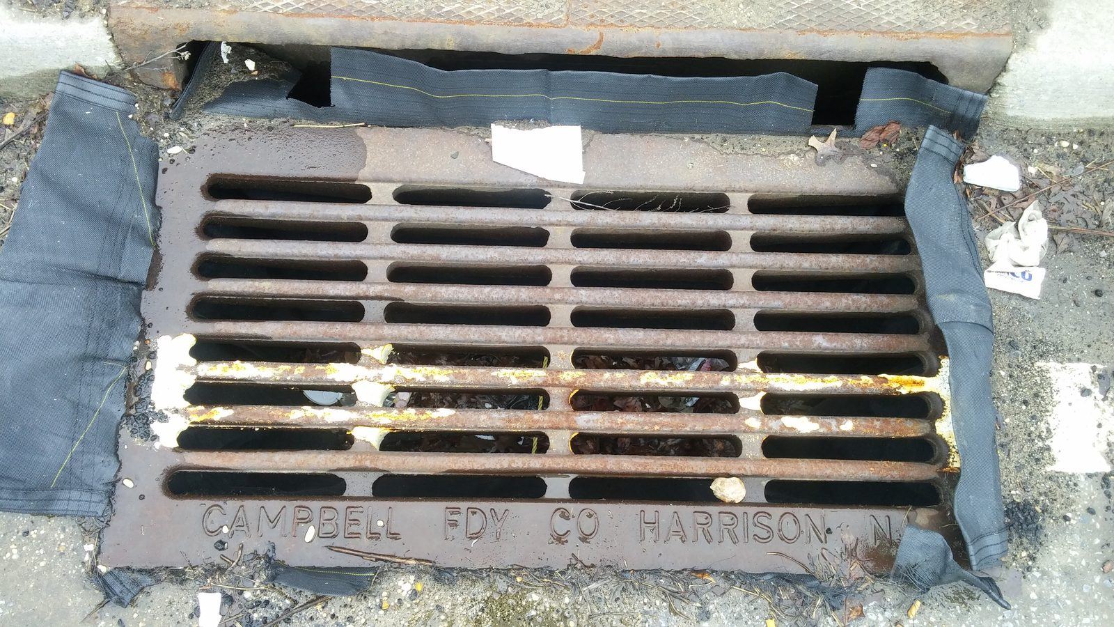 Catch-basin insert: a sediment-capture bag suspended beneath a street storm grate to trap debris and sediment