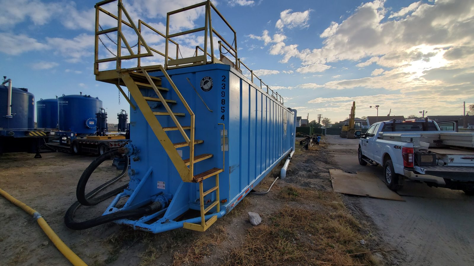 Row of blue groundwater treatment vessels and bag-filter units staged on a flatbed trailer for a construction dewatering operation