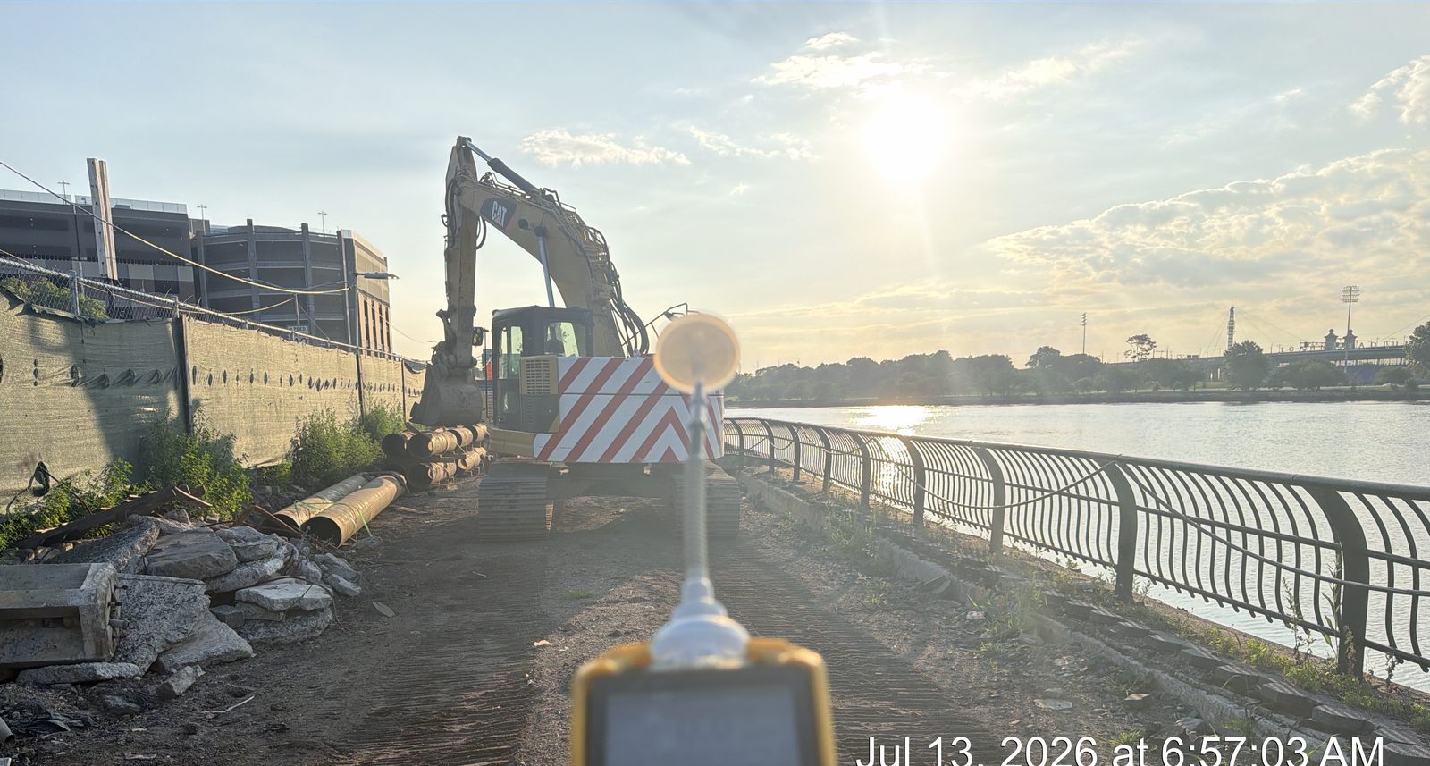 AMC field technician holding a photoionization detector (PID) to monitor air quality during soil-disturbance work at a waterfront construction site